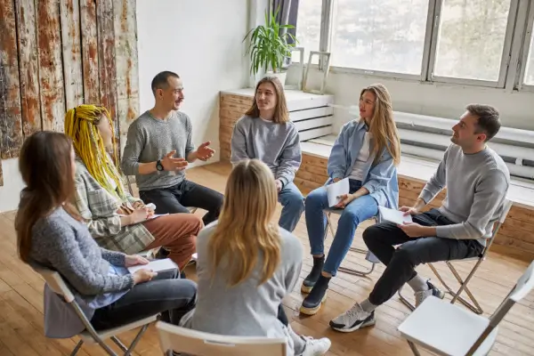 Group-of-people-in-alcohol-support-group-sit-in-a-circle-and-speak-to-one-another