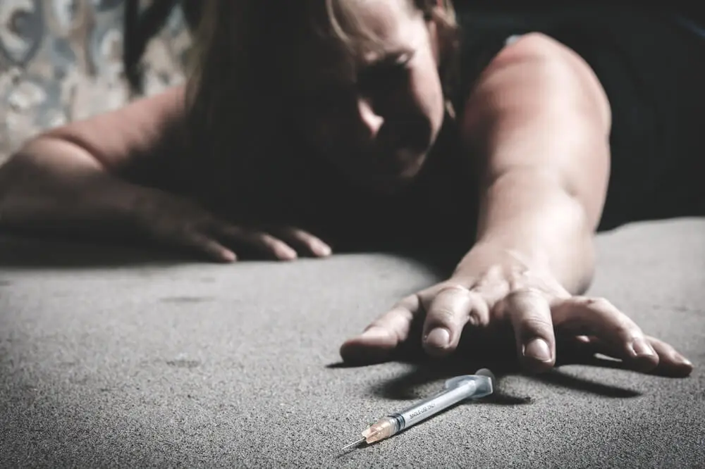 Person struggling with heroin addiction reaching toward a syringe, highlighting the need for professional heroin rehab and treatment