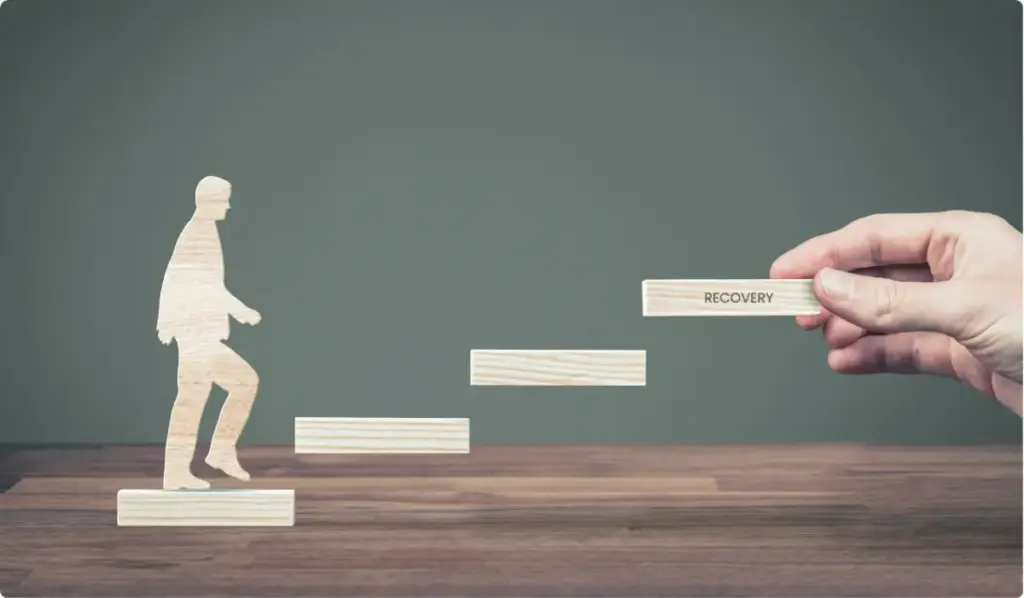 erson silhouette stepping upward while a hand adds a “Recovery” block, representing addiction recovery and staying sober.